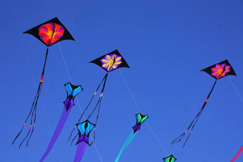 Воздушные змеи с геометрическими рисунками и хвостами на фоне голубого неба